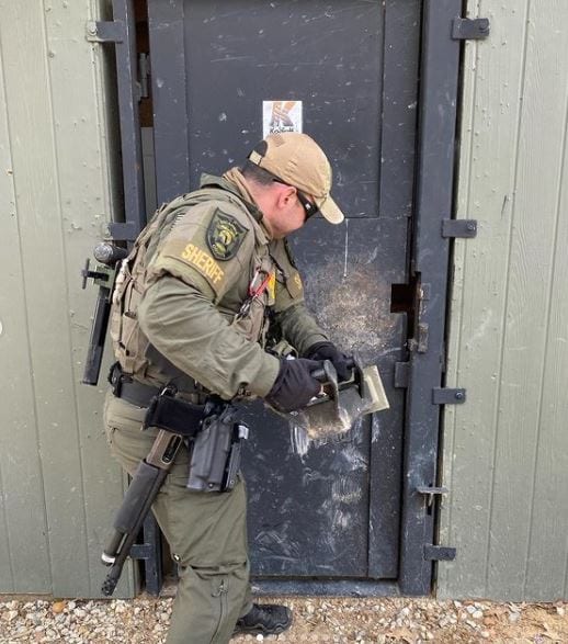 A police officer opening a door with a BREACHING RAM TR-1CQ.