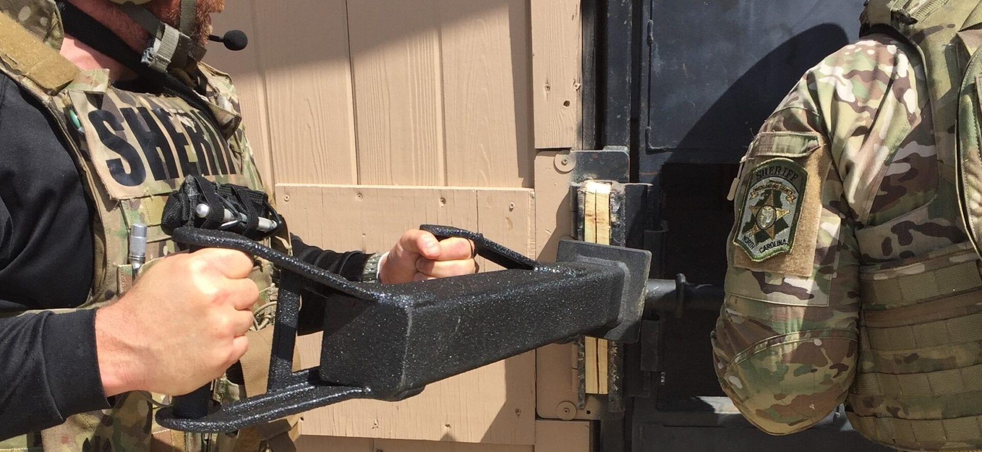 A man in a military uniform is using the TR-1 BREACHING RAM to open a door.