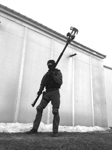 A man holding the RDT - RECON SCOUT ROBOT DELIVERY TOOL in front of a building.